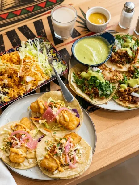 Table of fish and carnitas tacos with Mexican rice and black beans at MEXIKAN in Chappelle, Edmonton